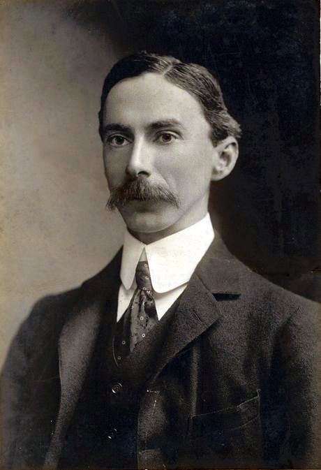 Photograph of a young man with a moustache in a dark suit and high collar