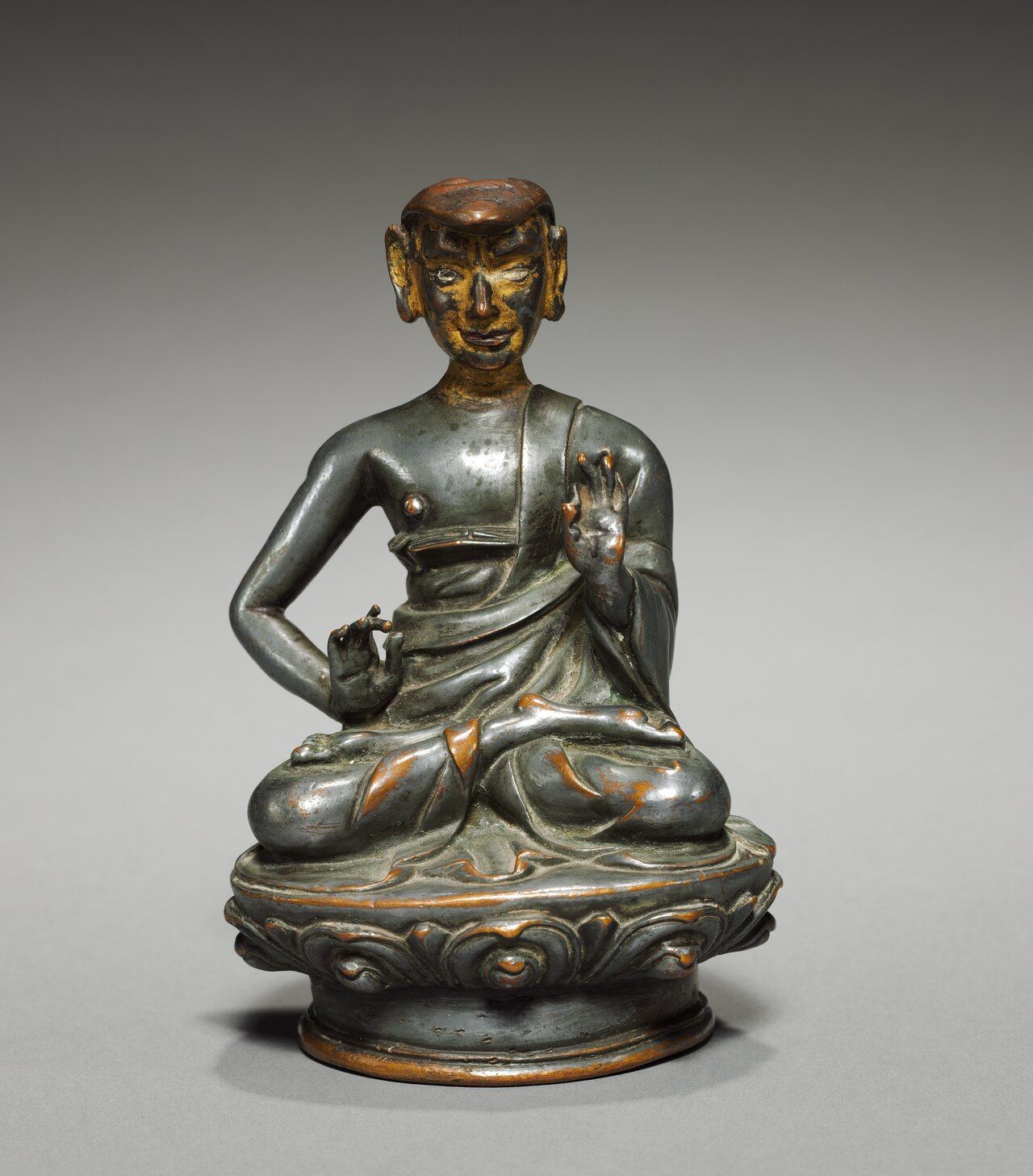 Gilt metal figure of a seated monk with one hand raised