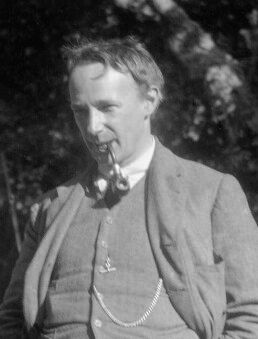 Photograph of a man smoking a pipe, in a tweed suit with a watch chain, outdoors
