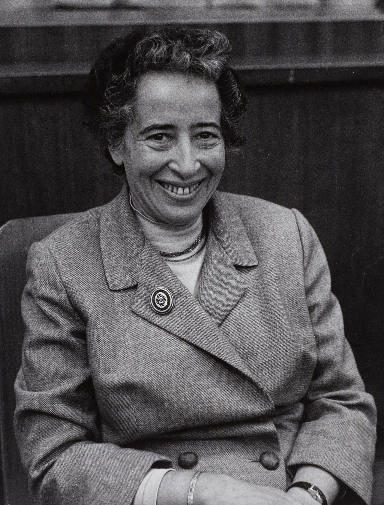 Black and white photograph of a smiling woman with short dark hair, wearing a suit and a brooch