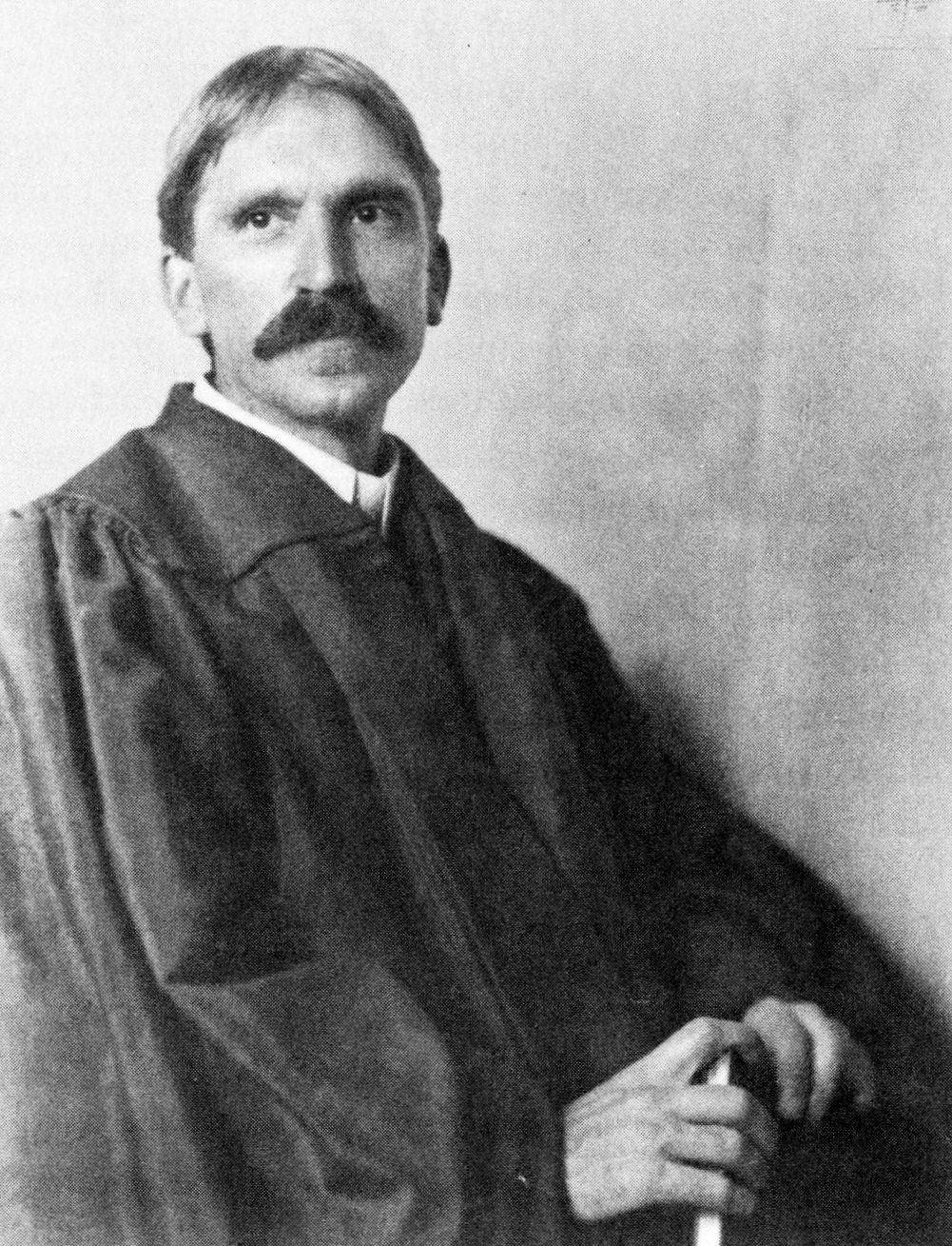 Photograph of a man with a moustache in an academic gown, seated