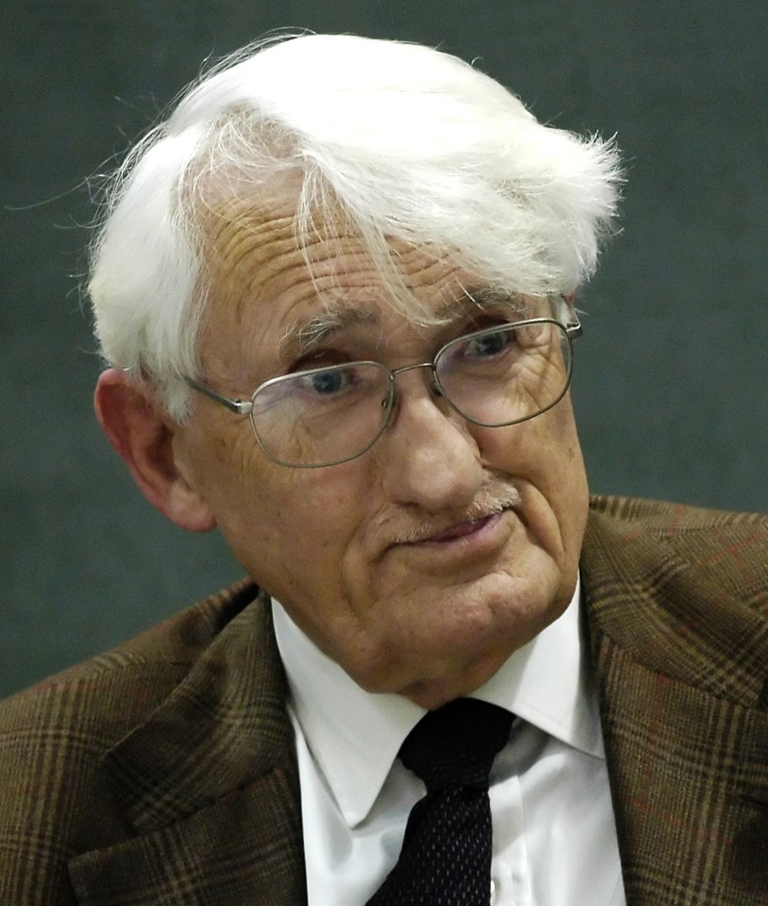 Colour photograph of an elderly man with white hair and glasses in a tweed jacket
