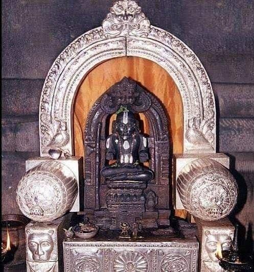 Dark stone image of a seated figure in an ornate silver shrine