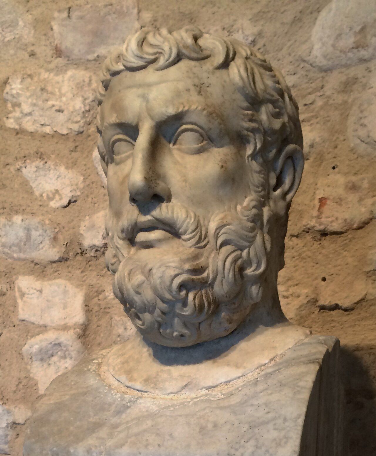 Weathered marble bust of a man with curly hair and a full beard