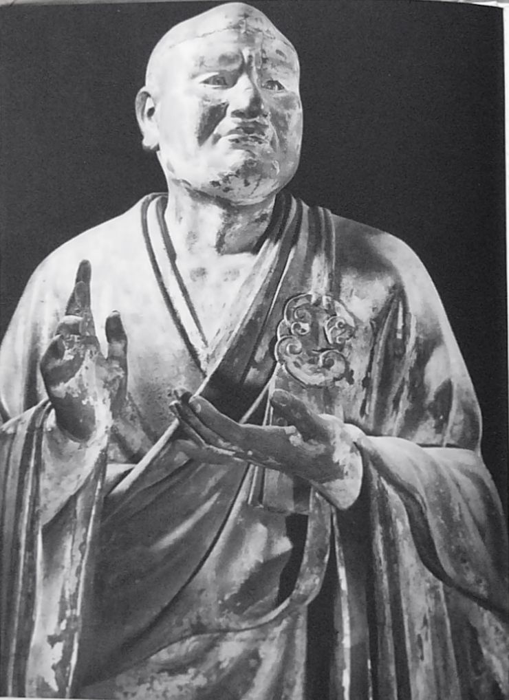 Photograph of a lifelike wooden statue of a monk with one hand raised
