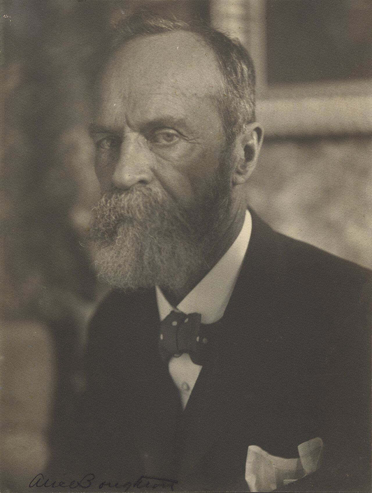 Photograph of an older man with a grey beard in a dark suit and bow tie